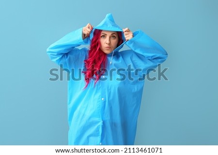 Funny woman with bright hair wearing raincoat on color background