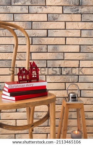 Chair with books and glowing candles near brick wall in room. Christmas story