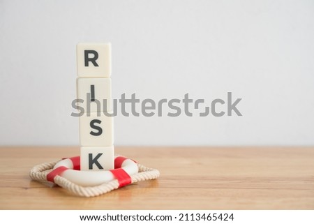 Word RISK is protected by red lifebuoy on wooden table white wall background copy space. Insurance business (life, health, property), risk management or assessment concept. Insurance is future guard.