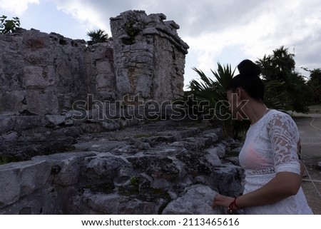 Young tourist woman enjoying the Mayan Riviera and her tropical iguana at the Mayan ruins of Tulum, Yucatan (Mexico). Turquoise water typical of the caribbean sea and a blue sky.