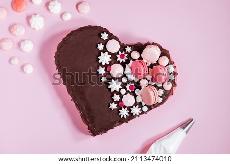 Top view of Pink heart shaped cake with chocolate glaze, meringues and macaroons on top as decoration. Placed on pink background. Valentine's day, mothers day, birthday, celebration concept. Royalty-Free Stock Photo #2113474010