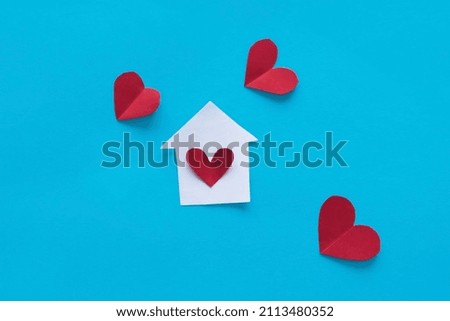 Miniature house and a red heart made of paper on a blue background. Concept of family, insurance, mortgage. Top view, copy space.