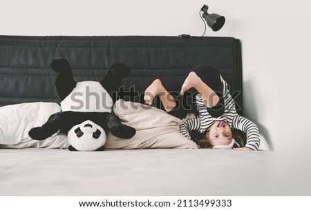 Happy little girl playing with soft big plush panda at home. Concept of family, healthy sleep of child, upbringing, parenting. Сhildhood and friendship.