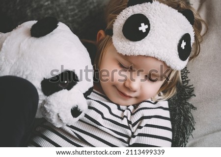 Cute little girl hugging with soft big plush panda at home. Concept of family, healthy sleep of child, upbringing, parenting. Сhildhood and friendship.