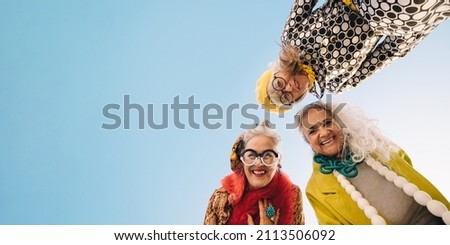 Low angle view of happy senior women smiling at the camera outdoors. Group of cheerful elderly women wearing colourful casual clothing. Three stylish senior women enjoying their golden years. Royalty-Free Stock Photo #2113506092