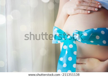 pregnant woman with a big belly ties a blue ribbon