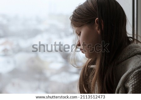 Sad Depressed Teen Girl sitting Alone and Depressed on the windowsill. Unhappy teenager is upset with negative thoughts. Help children. Royalty-Free Stock Photo #2113512473
