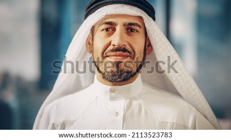 Portrait of Successful Arab Businessman in Traditional Outfit Gently Smiling, Wearing White Kandura and Black Agal Keeping a Ghutra in Place. Saudi, Emirati, Arab Businessman Concept. Royalty-Free Stock Photo #2113523783