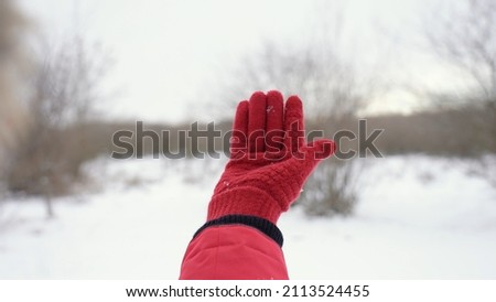 Close-up first person view photo of one empty gloved raised female hand isolated on white snowy winter landscape background. Woman catching snoflakes and playing with them. Happy winter cold season