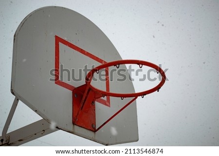 Old basketball hoop and backboard on the background of falling snow and cloudy sky