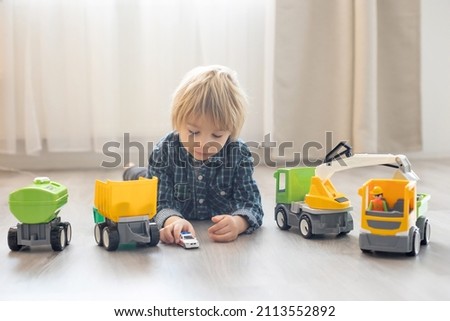 Cute toddler blond child in front of a teepee, playing with big cars on the floor, enjoying games