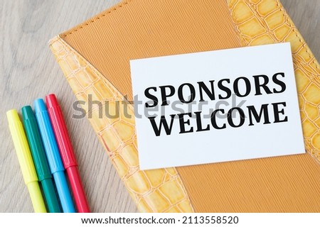 Sponsors Welcome text on a white card on a notebook on a wooden fnoe row color markers