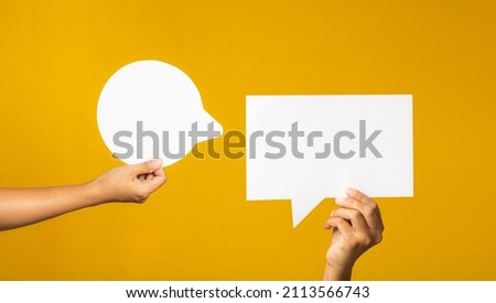 A speech bubble concept. Hand holding of an empty white speech bubble against a yellow background. Space for text. Close-up photo.