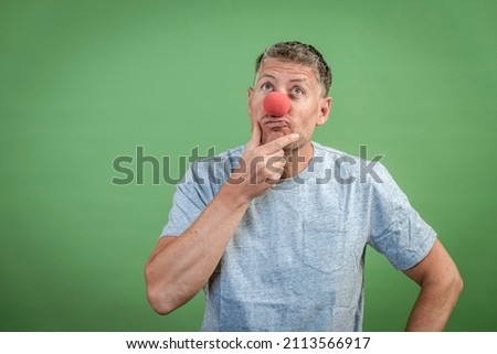 man with red clown nose and grey shirt in front of green background