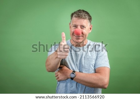 man with red clown nose and grey shirt in front of green background