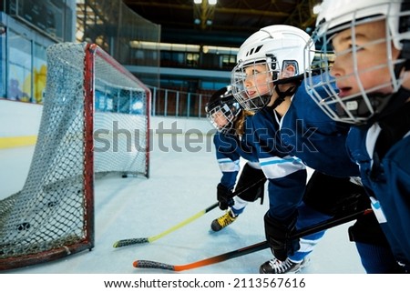 Cute boy learning to ice skate and play hockey with his couch at indoors rink. Staying next to goal and holding hockey stick