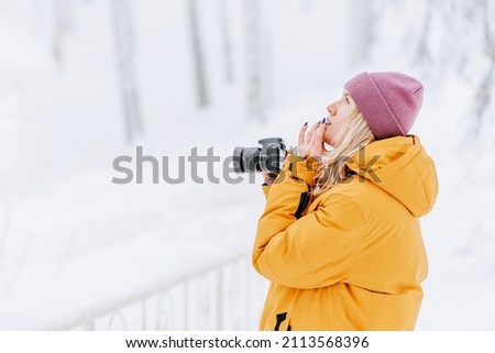Positive girl in yellow jacket photographer taking pictures of snow in winter park