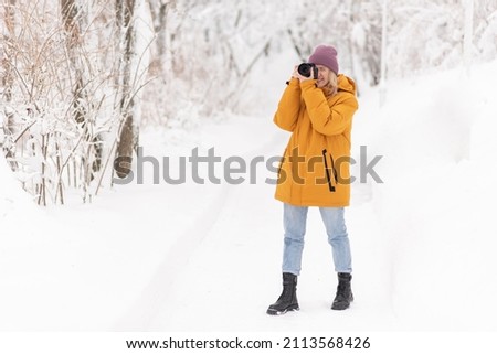 Cheerful girl with a camera in her hands takes pictures of winter in a snowy park