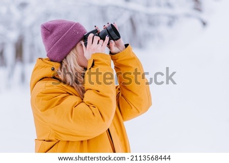 Cheerful girl photographer takes pictures of winter in a snowy park