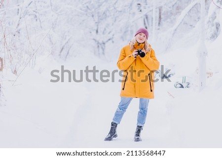 Cheerful girl photographer takes pictures of winter in a snowy park