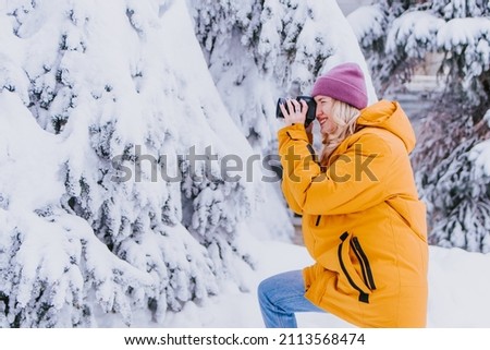 Cheerful girl with a camera in her hands takes pictures of winter in a snowy park