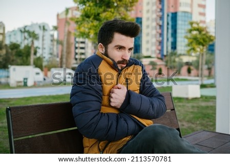 Cold man, the young bearded man is cold outside and puts on his coat, a cold male reaction on a cold winter day