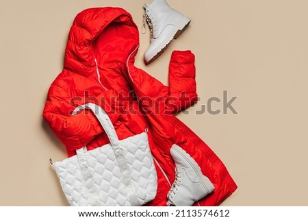 Red  jacket with white quilted bag and boots on beige background. Fashion outfit, casual youth style, sports. Stylish autumn or spring  clothes.