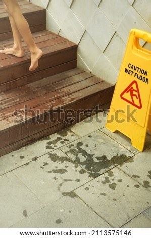 Wet floor sign board placed beside wooden stairs at swimming pool with a child stepping up the stairs