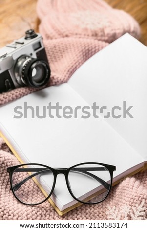 Eyeglasses and opened book with blank pages on winter clothes, closeup