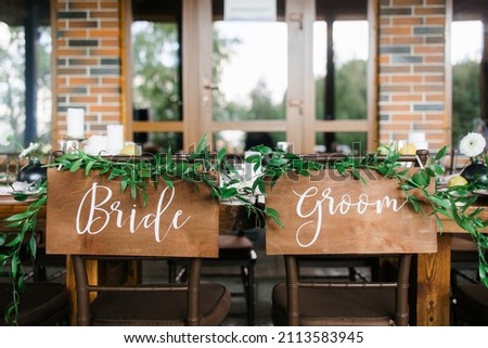 Wooden chairs at the table. The sign of the bride and groom on the chairs. Luxury jewelry for the wedding day. the inscriptions of the bride and groom are decorated with fresh eucalyptus leaves.