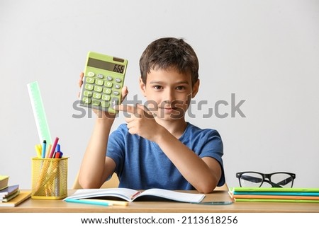 Little boy with calculator doing homework at table on light background
