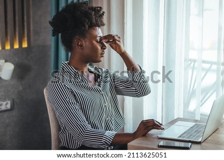 Young frustrated woman working at desk in front of laptop suffering from chronic daily headaches, treatment online, appointing to a medical consultation, electromagnetic radiation, sick pay