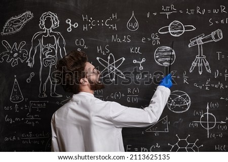 A smart enthusiastic scientist stands at the blackboard explaining  scientific formulas and diagrams. Science and education. Royalty-Free Stock Photo #2113625135