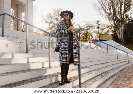 portrait of attractive young woman walking in autumn street wearing checkered black and white coat, black hat, happy mood, fashion style trend, black friday sale, sunny sunglasses