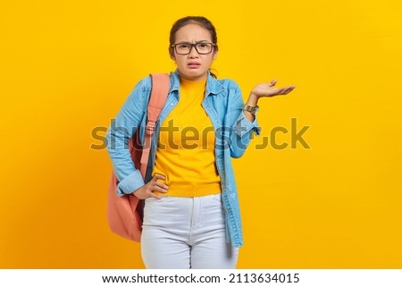 Confused young Asian woman student in denim outfit with backpack saying no with palms isolated on yellow background.  Education in university college concept
