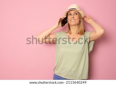 Young smiling woman in straw hat using smartphone standing isolated over pink background.