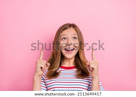 Photo of impressed teenager girl look up wear striped t-shirt isolated on pink color background