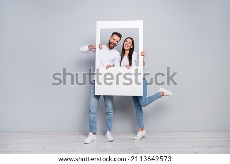 Full length body size view of attractive cheery couple holding photo frame having fun isolated over grey pastel color background