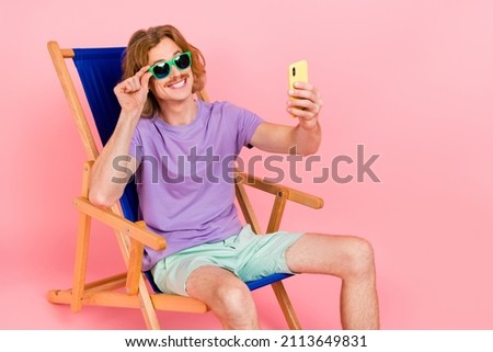 Portrait of handsome trendy cheery guy sitting in chair taking selfie touching specs isolated over pink pastel color background