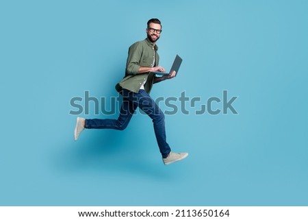 Profile photo of sporty active guy jump hold netbook run work wear specs green shirt isolated blue color background Royalty-Free Stock Photo #2113650164