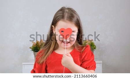 funny Little girl in a red dress with a heart on a stick closes their eyes. Valentines day concept.