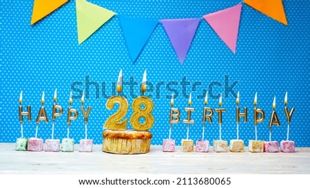 Congratulations on your birthday from the letters of the candles number 28 on a blue background with polka dots white copy space. Happy birthday muffin with burning golden color candle for twenty eigh