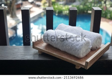 A small white towel neatly rolled up on a wooden plank in a pool background            