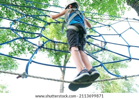 Child boy having summer fun at adventure park on the zip line. Balance beam and rope bridges Royalty-Free Stock Photo #2113699871