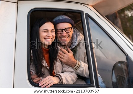 Handsome man and charming woman embracing and looking from the car with inspiration. Camping concept. Stock photo