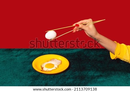 Woman's hand tasting fried eggs with chopsticks isolated on green and red background. Vintage, retro style interior. Food pop art photography. Complementary colors, Copy space for ad, text