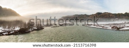 Aerial Panoramic View of Chilliwack River with snow during winter season. Cloudy Sunset Sky. Fraser Valley, British Columbia, Canada. Royalty-Free Stock Photo #2113716398