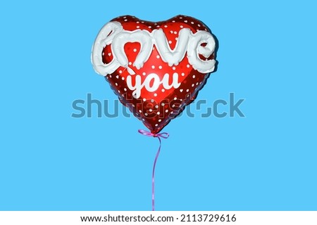 An inflated red foil heart-shaped balloon with the sign love you as a symbol of love and Valentine's Day on a blue background.