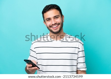 Young Brazilian man isolated on blue background using mobile phone Royalty-Free Stock Photo #2113734599