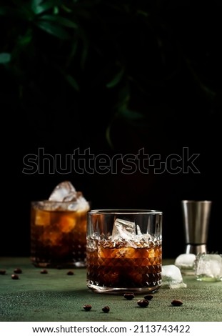 Black russian cocktail, trendy alcoholic drink with vodka, coffee liqueur and ice, rusty green background, bar tools, copy space